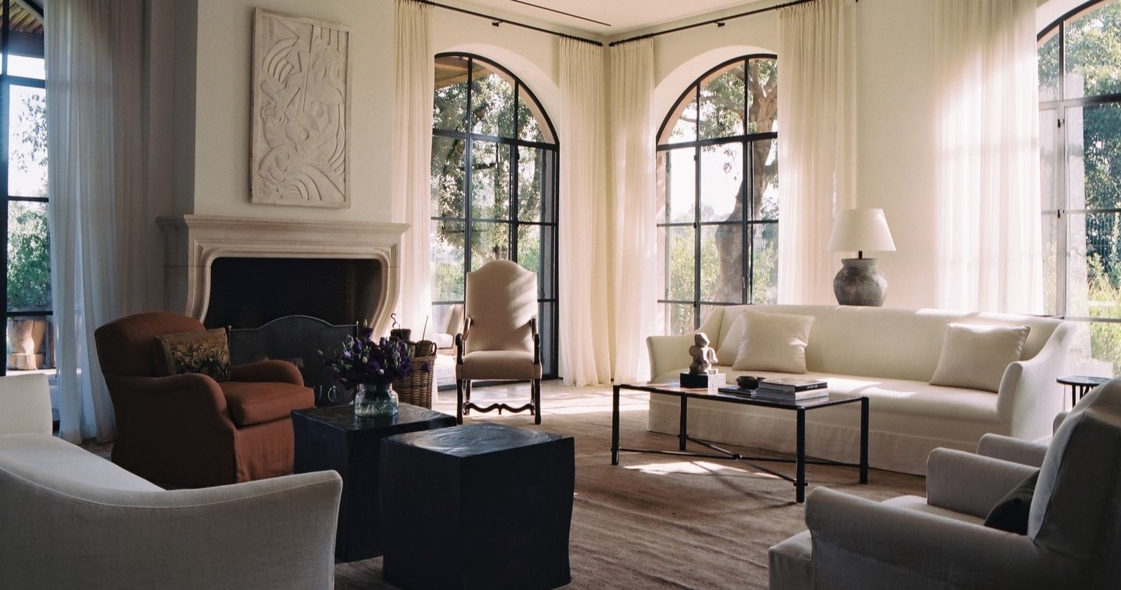 Sunlit living room with arched steel windows, a limestone fireplace and a cream sofa, designed by Kevin Spearman