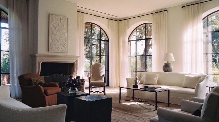 Living room with arched steel windows, a limestone fireplace, a cream sofa and a terracotta armchair