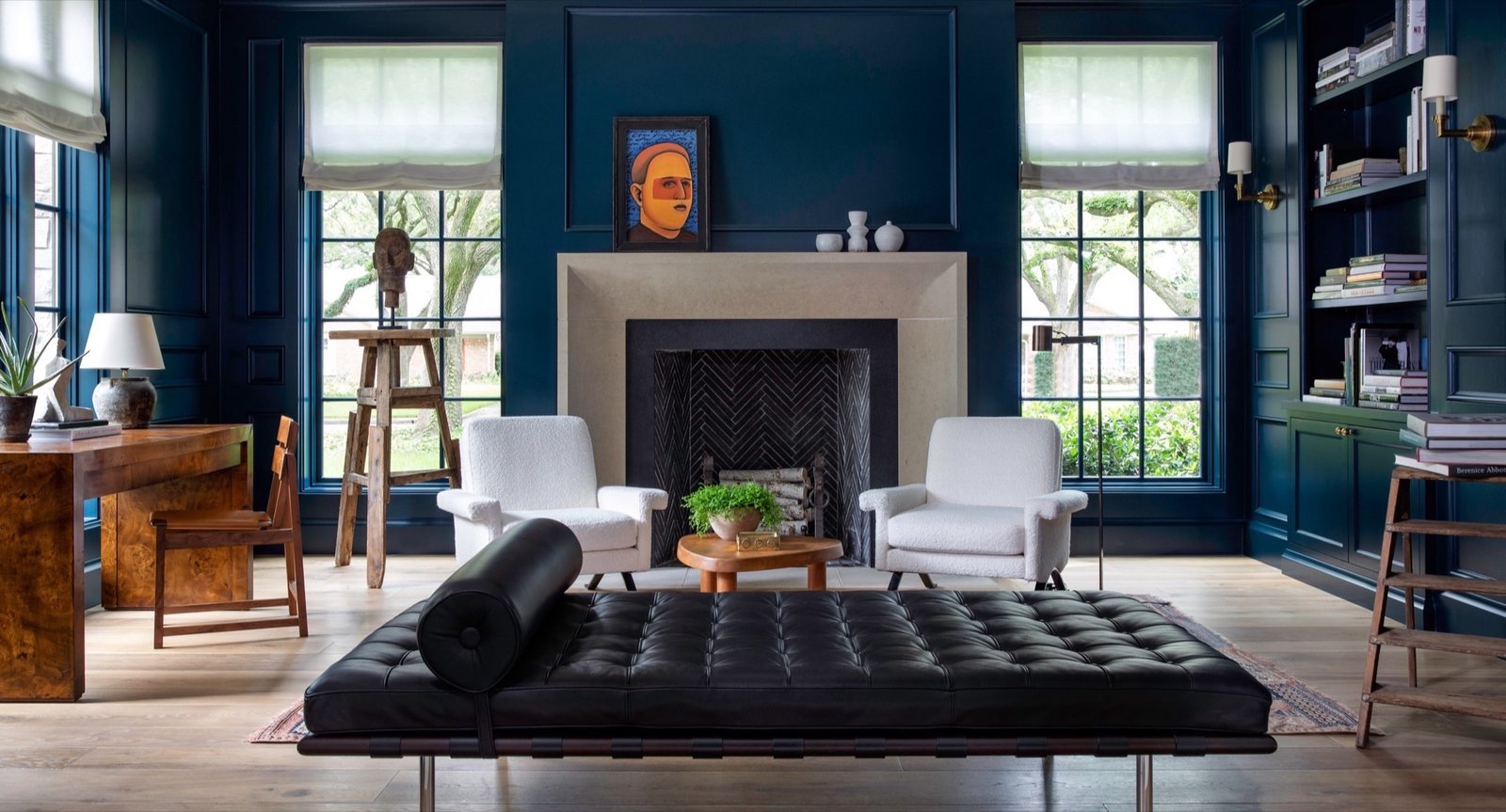 Deep navy paneled study with a black leather daybed, white boucle chairs and a limestone fireplace
