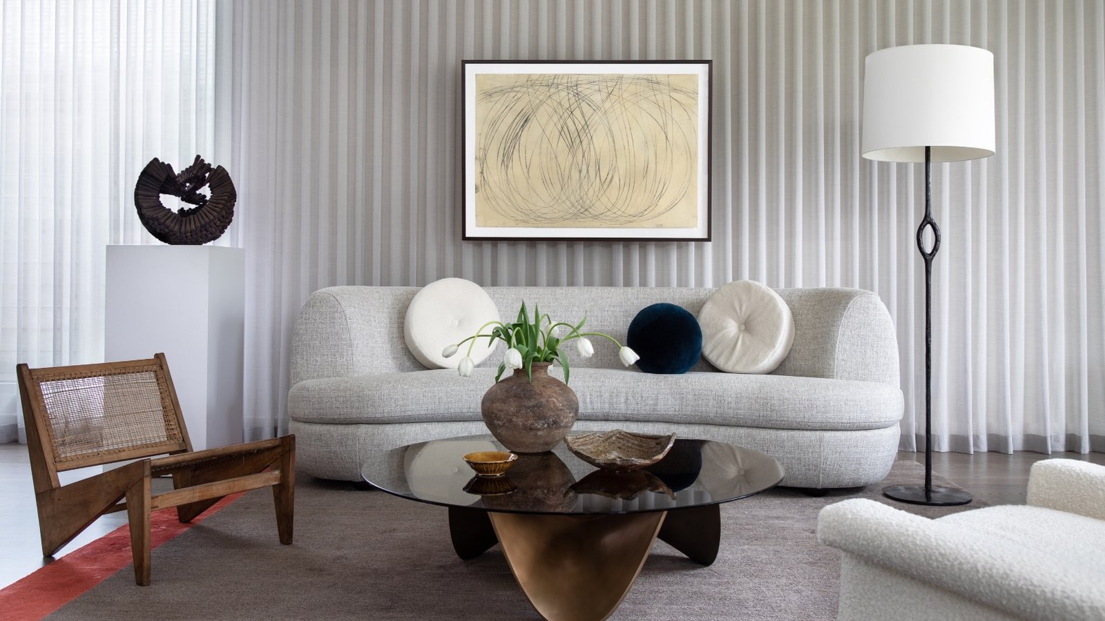 Soft contemporary sitting room with a curved grey boucle sofa, sheer drapery and a bronze and glass coffee table