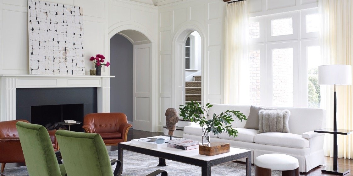 Bright paneled living room with green velvet chairs, cognac leather seating and arched doorways