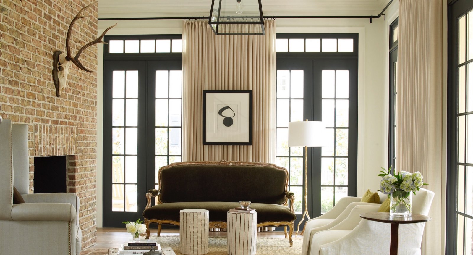Salon with an exposed brick fireplace, an antique green mohair settee and floor to ceiling drapery