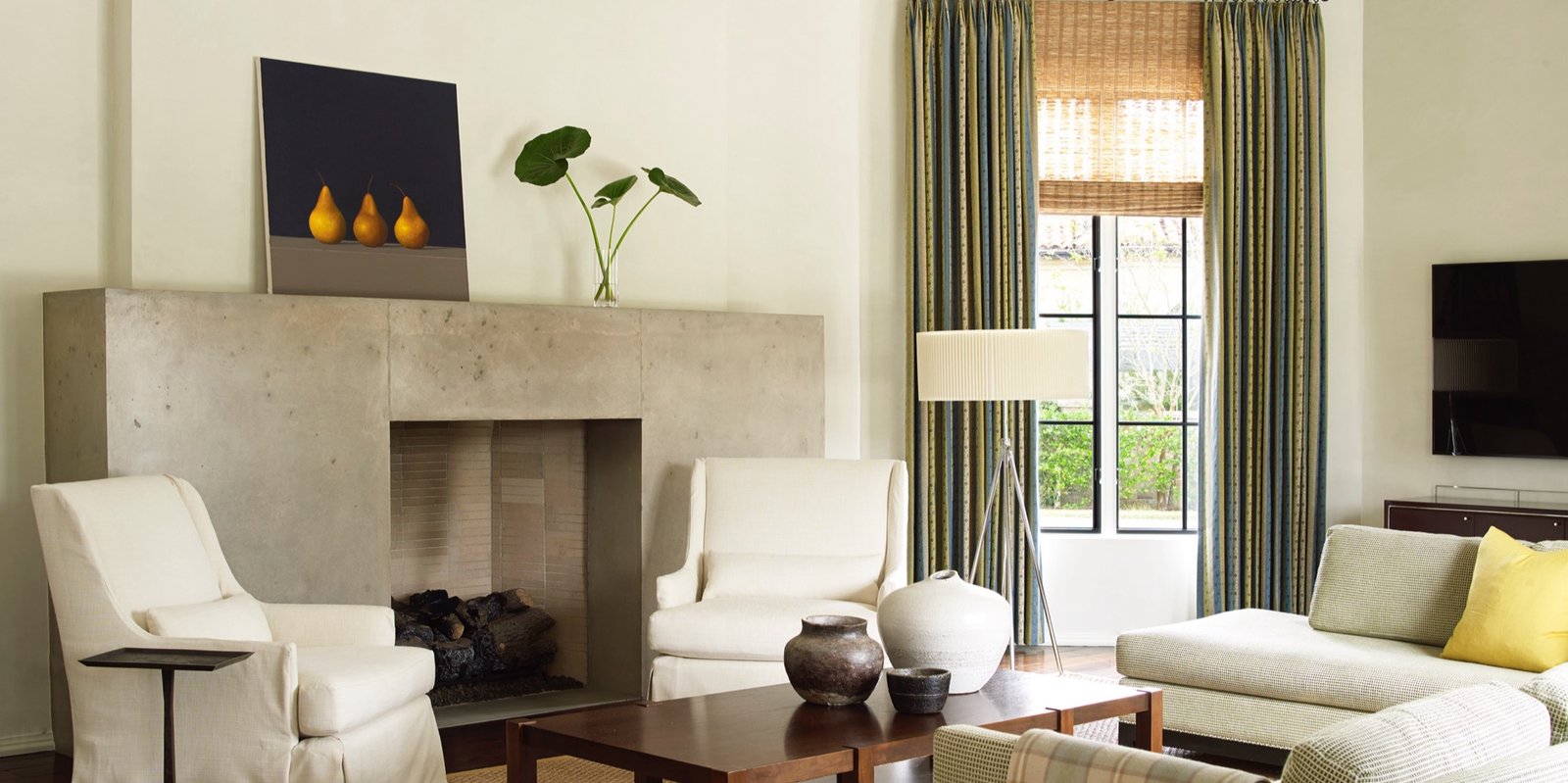 Serene living room with a poured concrete fireplace surround, cream slipper chairs and striped drapery