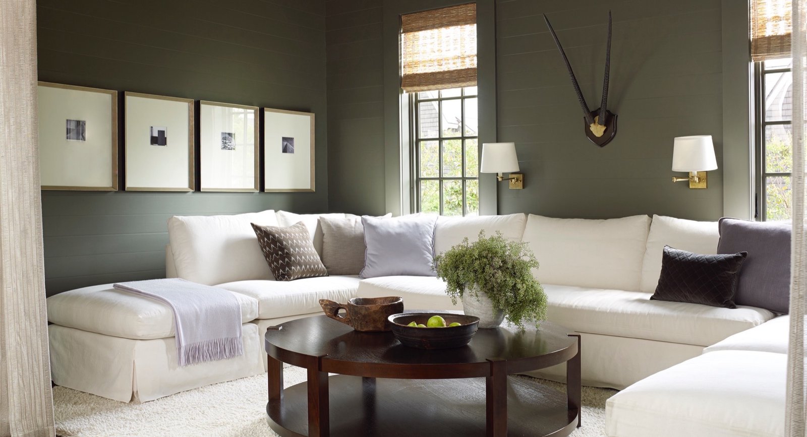 Cozy den with olive green shiplap walls, a white slipcovered sectional, brass sconces and a gallery of art